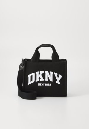 Črna torba iz blaga z belim logotipom "DKNY NEW YORK". Ima dvojne ročaje in odstranljiv trak. Pravokotna oblika z teksturirano površino.