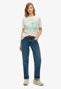 Grå t-shirt med grafik af turkise bjerge, parret med blå jeans og beige sneakers. Casual pasform, enkelt design med rund hals.