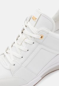 Baskets blanches en cuir et mesh avec lacets blancs, œillets dorés et logo MK doré sur la languette, marquage embossé Michael Kors sur le côté.