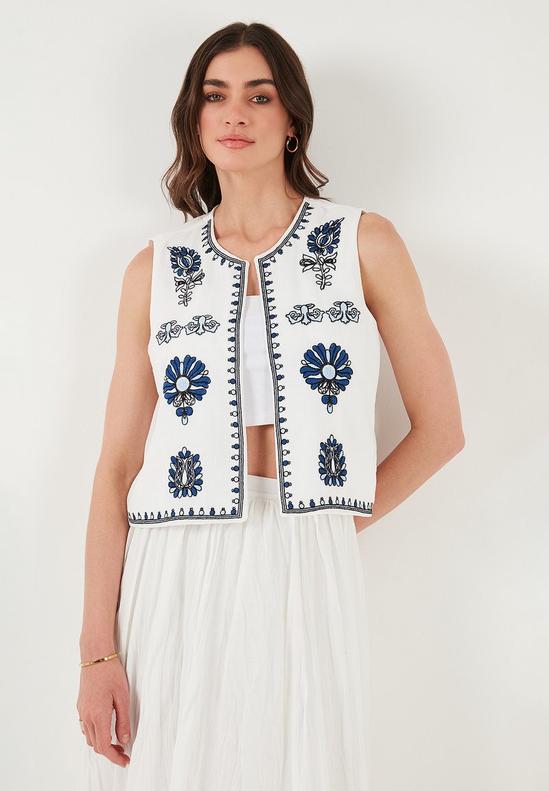 Gilet sans manches blanc avec broderie florale bleue et accents. Doté d'un col rond, d'une ouverture à l'avant et d'un détail complexe le long des bords.