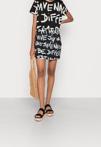 Top gráfico negro y falda con texto blanco, bolso de fibras tejidos y sandalias de plataforma negras. Tela de algodón, diseño casual, largo por encima de la rodilla.