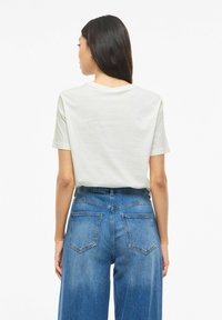 Jasnoszara koszulka z krótkimi rękawami i okrągłym dekoltem, połączona z wysokim stanem niebieskich jeansów z dwoma tylnymi kieszeniami.