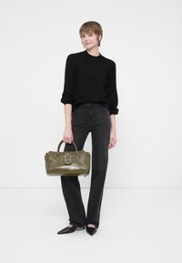 Black textured sweater, high-waisted black jeans, pointed black heels, and a green leather bag with a star detail and silver accents.
