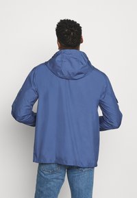 Mörkblå, lätt jacka med huva, som har en slät yta och långa ärmar. Inkluderar axeldetaljer och en avslappnad passform.