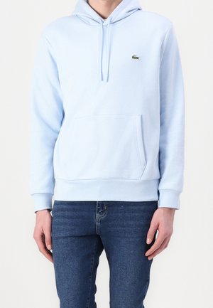 Hellblauer Hoodie mit einer vorderen Tasche, Kordelzugkapuze und kleinem grünen gesticktem Logo. Hergestellt aus weichem Stoff, mit gerippten Bündchen und Saum.