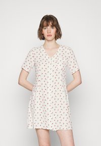 Vestido de cor clara com mangas curtas, decote em V e pequeno padrão floral vermelho. Possui um bolso frontal e um ajuste descontraído.