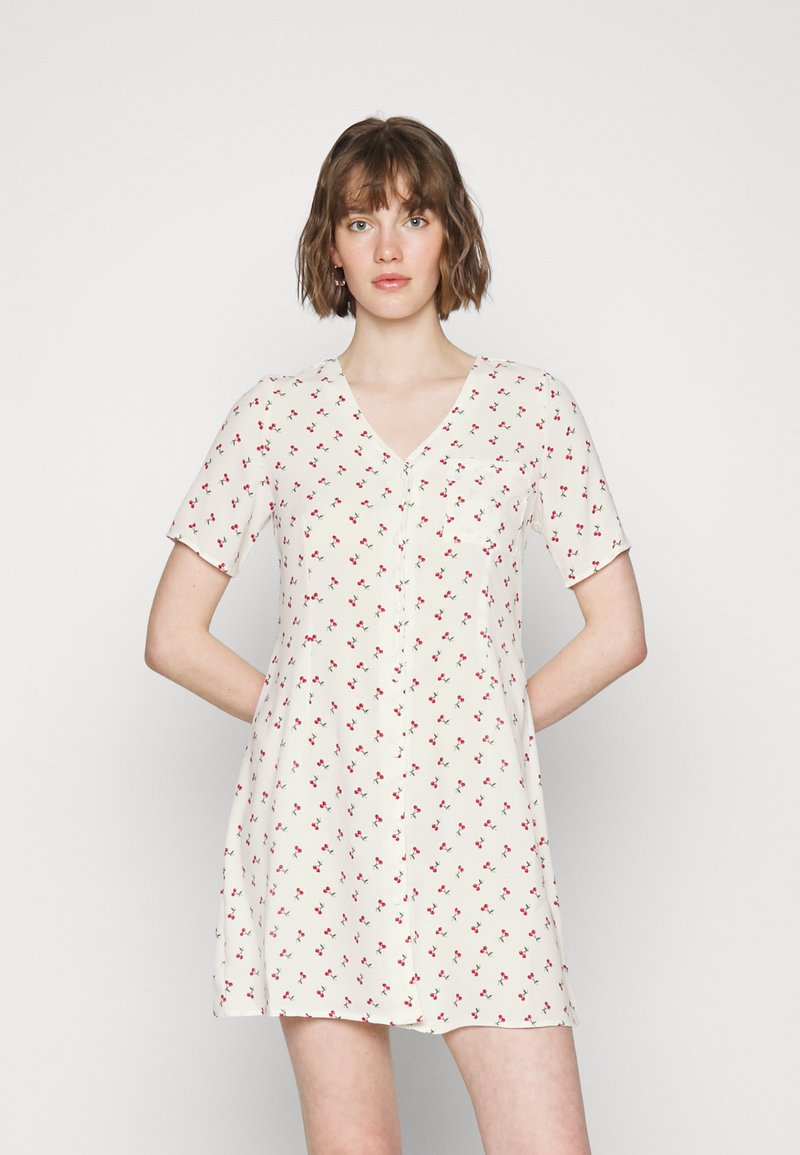 Vestido de cor clara com mangas curtas, decote em V e pequeno padrão floral vermelho. Possui um bolso frontal e um ajuste descontraído.