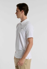 Camisa polo branca com mangas curtas, apresentando um colarinho e um pequeno logótipo cinza no lado superior esquerdo. Feita de tecido de algodão suave.