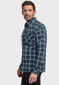 Herrenhemd mit Knopfleiste in dunkelblau mit hellblauem karierten Muster. Verfügt über zwei Brusttaschen und lange Ärmel. Hergestellt aus Flanellstoff.