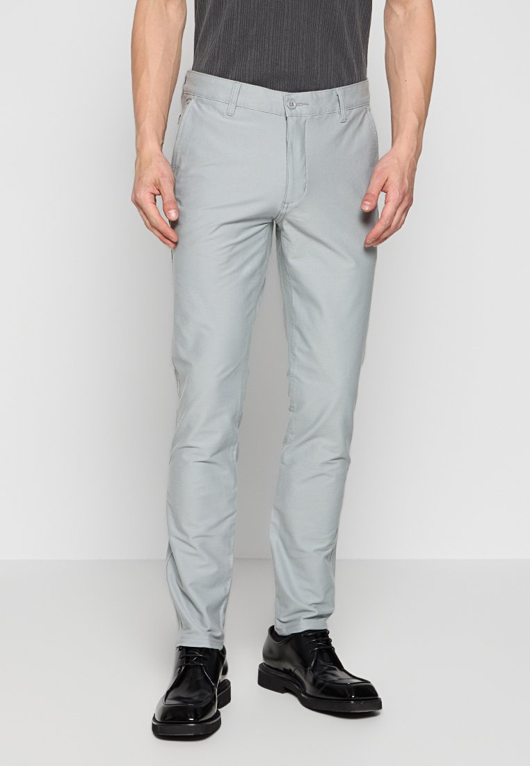 Lichtgrijze broeken van gladde stof, slim fit, met een standaard tailleband met knoopsluiting en voorzakken. Zwarte schoenen maken de outfit compleet.