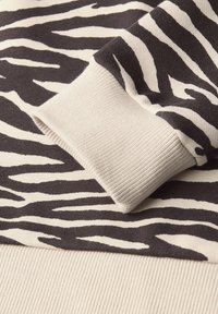 Zwart en crèmekleurige trui met een zebraprint, geribbelde manchetten en een zachte, gestructureerde stof. Close-up weergave van de materiaaldetails.