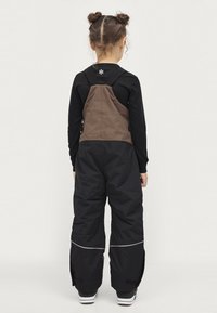Zwarte en bruine winteroverall met verstelbare schouderbanden, zijritsen en reflecterende accenten voor zichtbaarheid. Gemaakt van duurzame materialen.