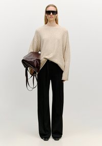 Beiger strukturierter Pullover, schwarze weite Hose und eine dunkelburgunderfarbene Ledertasche mit zwei Griffen. Das Model trägt schwarze Sonnenbrillen.