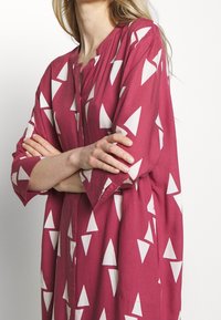 Fuchsian klänning med vita triangulära mönster, med rund halsringning, trekvartsärmar och avslappnad passform med sidofickor.