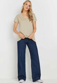 Beige v-ringad t-shirt med korta uppvikta ärmar, kombinerad med vida mörka denimjeans. Jeansen har blå sömmar och kontrastdetaljer.