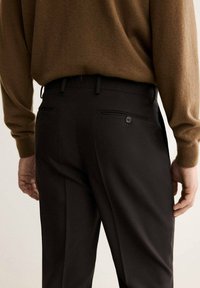 Pantaloni neri su misura con due tasche posteriori, dotati di un bottone sulla tasca destra e una finitura liscia e testurizzata.
