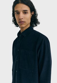 Marineblauw corduroy overhemd met knopen en een zakje aan de linkerkant van de borst, voorzien van een kraag en zichtbare textuur in de stof.