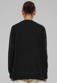 Jersey negro extragrande con cuello y puños acanalados, que presenta un tejido de punto texturizado. La espalda muestra un ajuste relajado y hombros caídos.