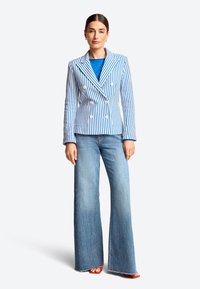 Blauw-witte gestreepte dubbel breasted blazer met brede revers, gecombineerd met een blauwe top en flare jeans in het blauw. Rode sandalen maken de look af.