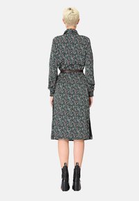 Robe à manches longues, à motifs sombres avec une taille ceinturée, présentant un design floral dans des couleurs douces. Associée à des bottines noires.