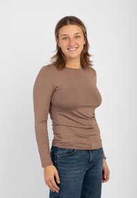 Maglietta marrone a maniche lunghe realizzata in tessuto morbido, con scollo rotondo e design aderente, abbinata a jeans blu.