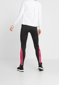 Leggings negros con paneles laterales a rayas rosas, detalles de cremallera en la pantorrilla, combinados con una blusa blanca de manga larga. Textura de tela suave.
