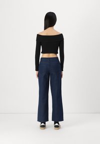 Černý žebrovaný crop top s odhalenými rameny ve spojení s tmavomodrými širokými džínami s vysokým pasem a dvěma zadními kapsami. Černobílé tenisky.