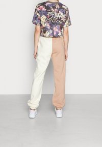 Korte mouw bloemetjes top, gecombineerd met kleurgelijke joggers in wit en beige. Witte sport sneakers maken de look compleet.