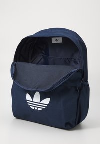 Laadukkaasta pehmeästä kankaasta valmistettu tummansininen reppu, jossa on valkoinen logo, läppäauko ja tilava sisus. Varustettu teksturoidulla pinnalla ja minimalistisella muotoilulla.