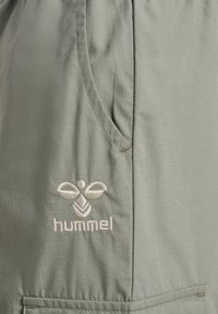 Lichtgroene stoffen shorts met een zijzak en geborduurd "hummel" logo in een lichtere tint. Glad textuur met zichtbare stikdetails.