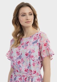 Blumenkleid mit kurzen, gerafften Ärmeln, einem hellblauen Hintergrund und pinken, lila und goldenen Blumenmustern, tailliert in der Taille.