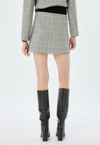 Gonna mini grigia in tweed con orlo frangiato, abbinata a stivali neri in pelle al ginocchio, che mettono in mostra una silhouette aderente e un materiale testurizzato.