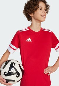 Rotes Kurzarmfußballshirt mit weißen Streifen an den Ärmeln und einem Logo. Ein schwarz-weißer Fußball wird mit einer Hand gehalten.