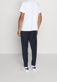 Witte korte mouwen T-shirt, marineblauwe tapse broek en witte sneakers met blauwe accenten, gezien vanuit de rug tegen een lichte achtergrond.