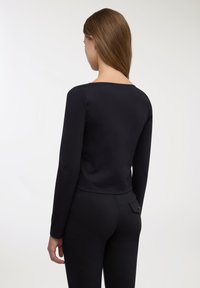 Top nero a maniche lunghe con vestibilità rilassata e scollo rotondo, realizzato in tessuto morbido e stretch. Design senza cuciture e senza elementi hardware visibili.