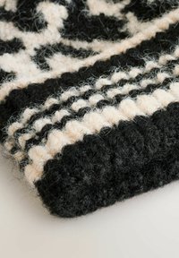 Strikket uldhat med et sort og creme mønster, der har strukturerede fibre og en tykk ribbet kant. Blød, fuzzy finish med et detaljeret design.