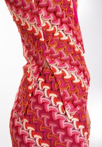 Vestido de ganchillo en tonos rosa y naranja, que presenta un patrón texturizado de elementos curvos, con una abertura lateral y detalles de espalda descubierta.