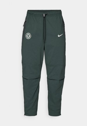 Pantaloni da jogging Nike verde scuro con vita elastica, cordino regolabile, cerniere laterali e logo del Chelsea FC sulla coscia sinistra.