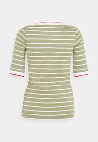 Koszula w oliwkowe paski z białymi poziomymi paskami, z czerwonym akcentem przy dekolcie i białym wykończeniem rękawów.