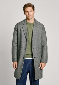 Abrigo de tweed gris con cuello muesca, diseño de un solo botón y botones azules, superpuesto a un suéter verde y jeans de mezclilla.