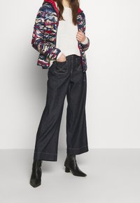 Kleurrijk gewatteerd jack met patroon, grijze trui, wijde donkerdenim broek en zwarte enkellaarsjes met blokhak.