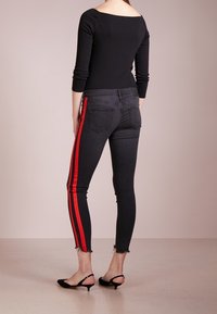 Svart långt ärmad topp i kombination med mörka jeans som har röda sidstripar och en fransad fåll. Utseendet kompletteras av svarta klackskor.