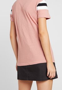 Rosa t-shirt med korta ärmar som har svarta och vita randiga detaljer på axlarna, kombinerad med en svart denimkjol.