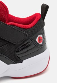 Černá a červená teniska s podpatkem a bílou podešví, s černým páskem, síťovinou a lesklými texturami, a červeným logem Jumpman.