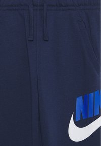 Tummansiniset collegehousut pehmeästä kankaasta, joissa on joustava vyötärönauha, kiristysnyörit, sivutaskut ja suuri valko-sininen Nike-logo.