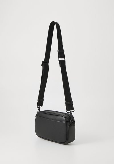 Sac bandoulière noir en simili cuir, de forme rectangulaire, avec une fermeture éclair et une sangle en tissu ajustable.