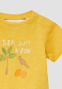 Geel peuter t-shirt met ronde hals en drukknoopjes op de schouders, versierd met een palmboom, vogel, sinaasappel, citroen en de tekst "ZEE, ZON & PLEZIER".