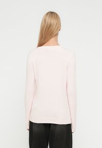 Camisola rosa clara com mangas compridas, bainha canelada e textura suave. Apresenta um decote redondo simples e um corte ajustado.