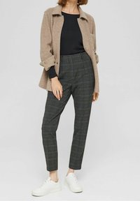 Beige wolmix jasje met knopen over een zwart topje, gecombineerd met geruite, hooggesneden broek in donkere tinten en witte sneakers.