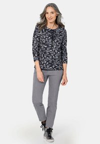 Navy top met wit bloemenpatroon, 3/4 mouwen, ronde halslijn en een strikaccent; gecombineerd met grijze rechte pantalon en metallic sneakers.